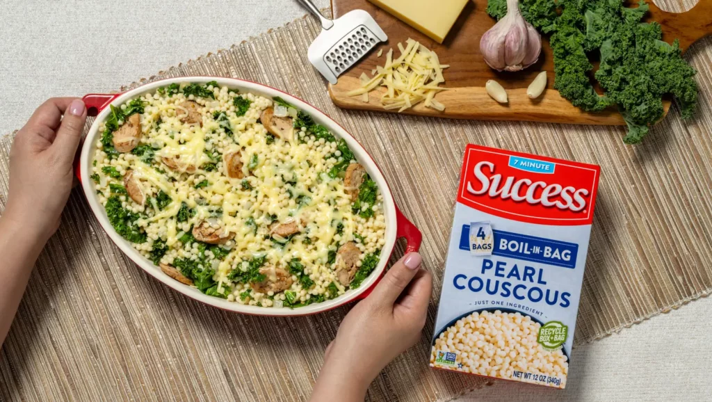 a pair of hands holding a bowl with baked pearl couscous with sausage kale and gruyere