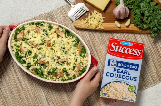 a pair of hands holding a bowl with baked pearl couscous with sausage kale and gruyere